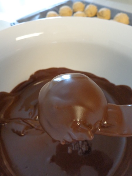 peanut butter cheesecake balls being dipped in a bowl of chocolate