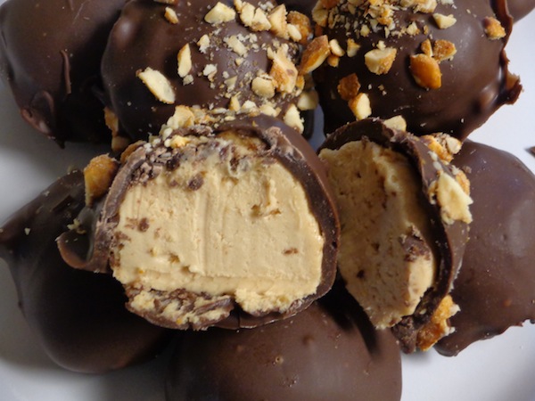 bowl of chocolate covered peanut butter cheesecake balls - ball on top is cut in half showing peanut butter mixture