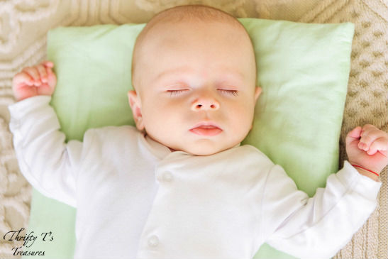 baby sleeping on a green pillow with his arms open wide