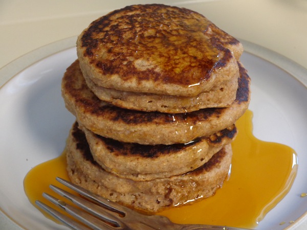 stack of four cinnamon applesauce pancakes covered in maple syrup