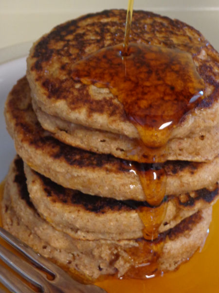 stack of four cinnamon applesauce pancakes with maple syrup being pour over them