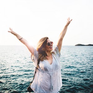 woman standing in front of ocean with hands in the air