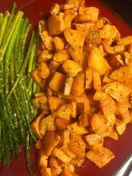 maroon colored plate topped with oven roasted sweet potatoes and garnished with roasted asparagus