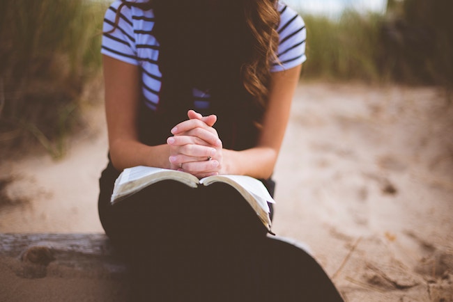 woman sitting on bench at beach praying with hands folded
